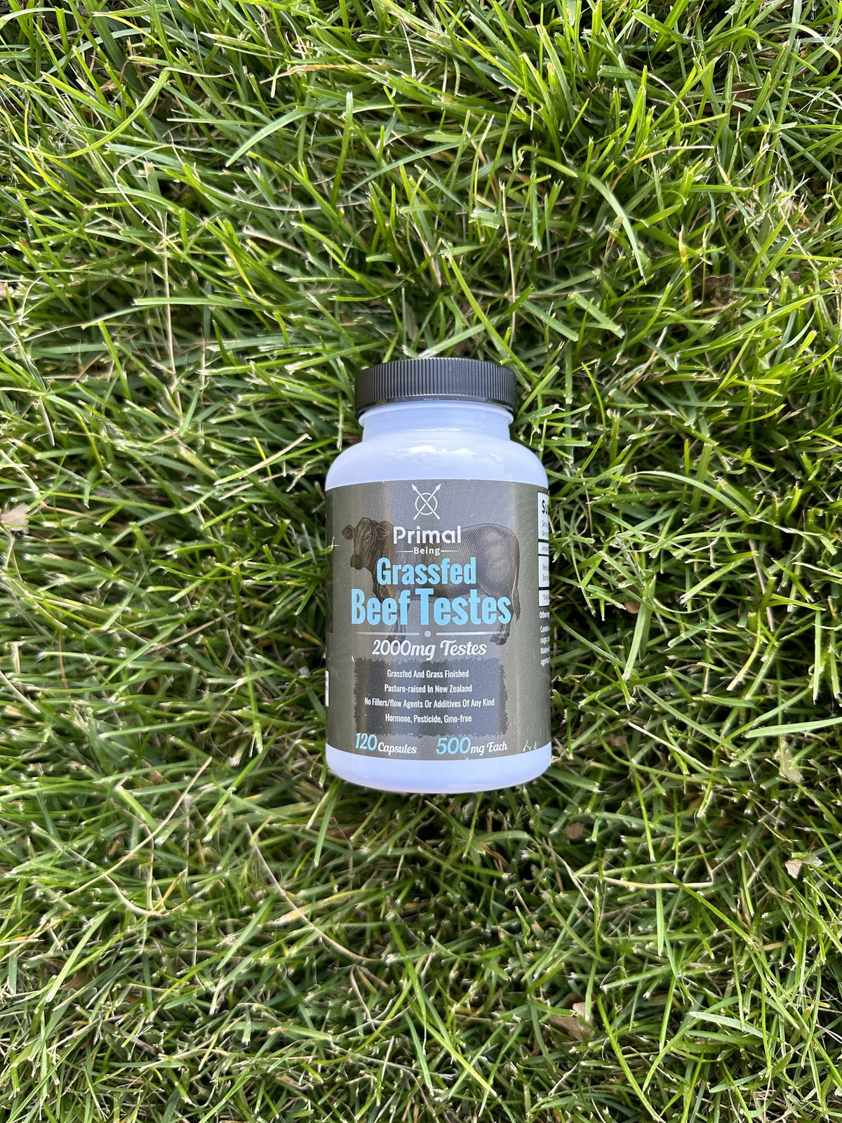 Primal Being Grass Fed Beef Testes bottle lying on green grass