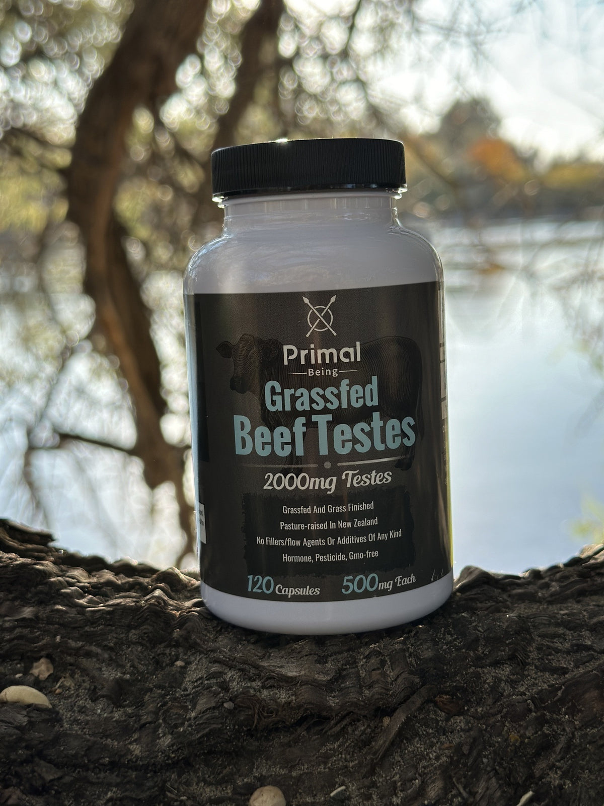 Primal Being Grass Fed Beef Testes bottle resting on a tree by a lake